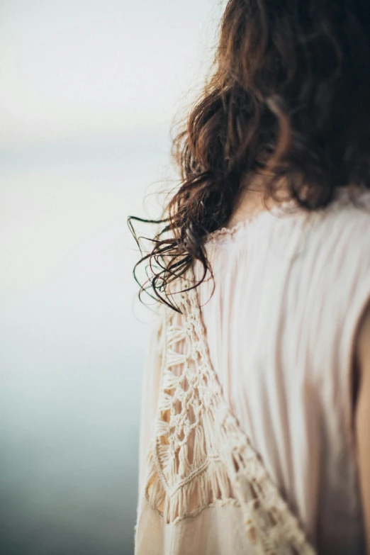 a woman with long hair and a white top looking at the ocean