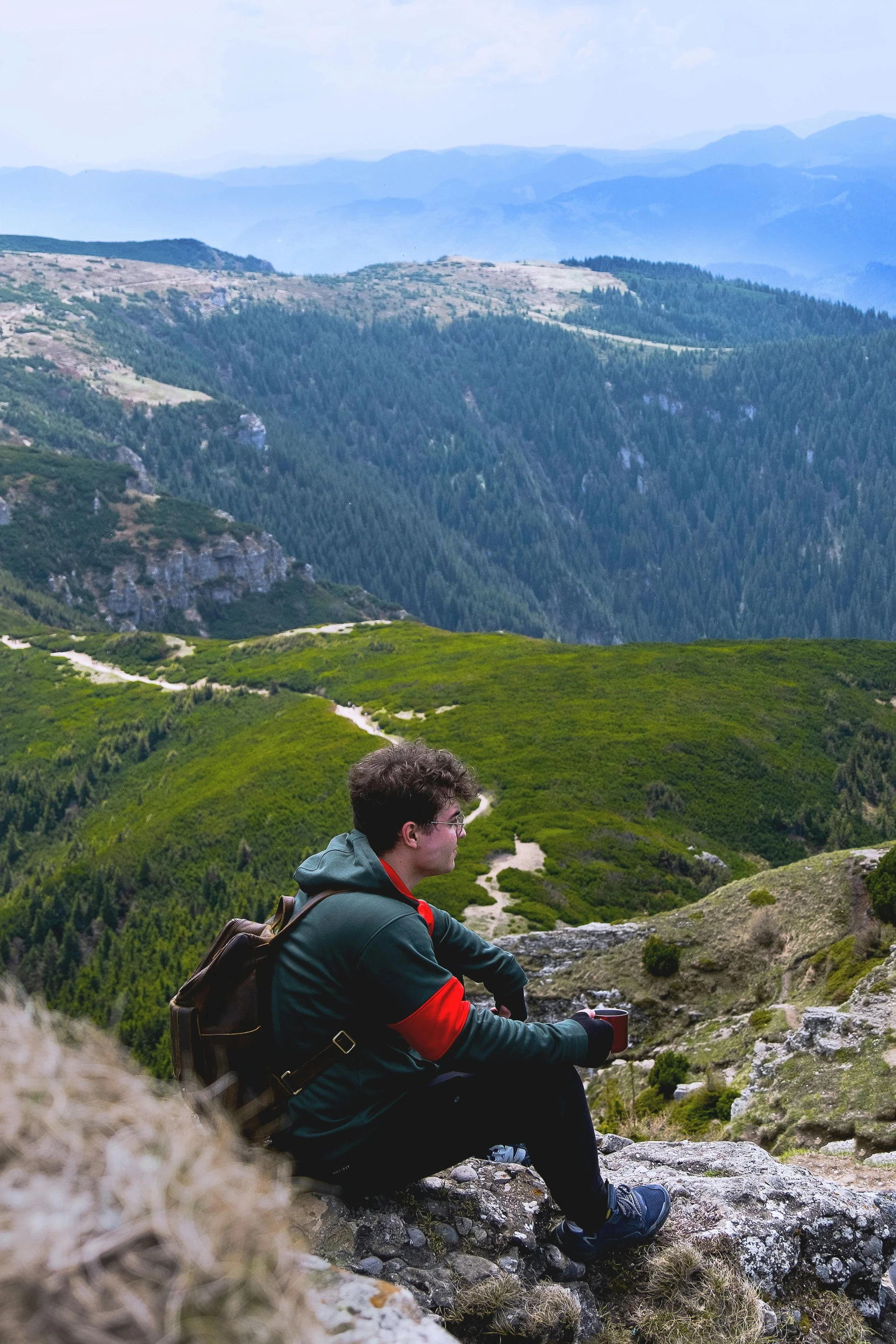 a guy sitting on the side of a hill looking at the mountains