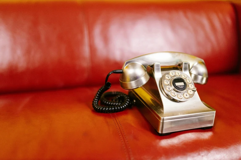 an old silver phone sits on a red leather chair