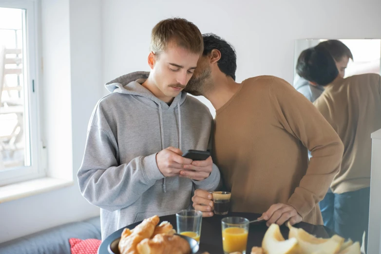 there are two men sharing a phone picture at the breakfast table