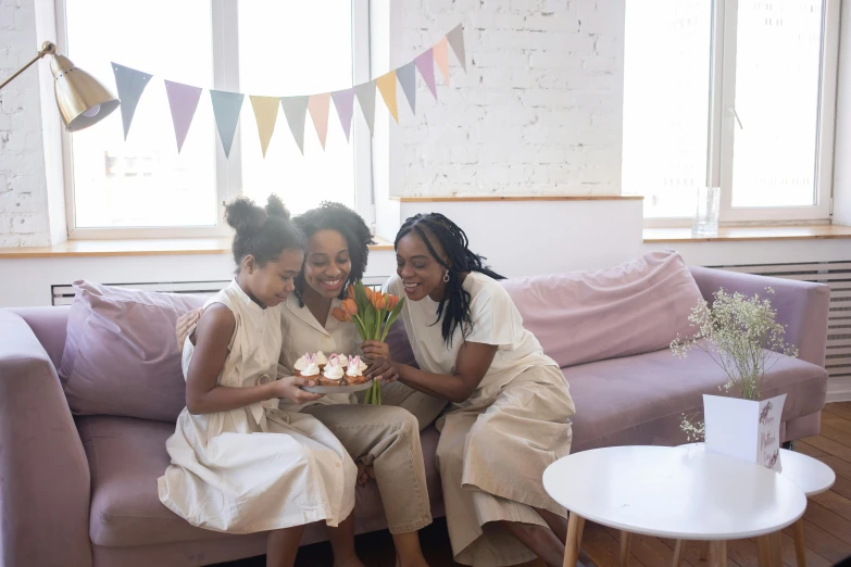 three women pose together in front of a pink couch and flag