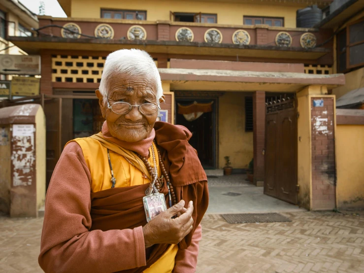 a older person in orange and yellow jacket standing next to a building