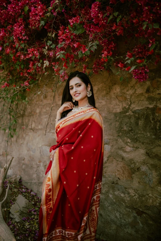 a beautiful woman in a red sari standing next to some flowers