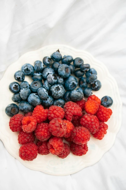 a plate full of berries and blueberries on top of a white table