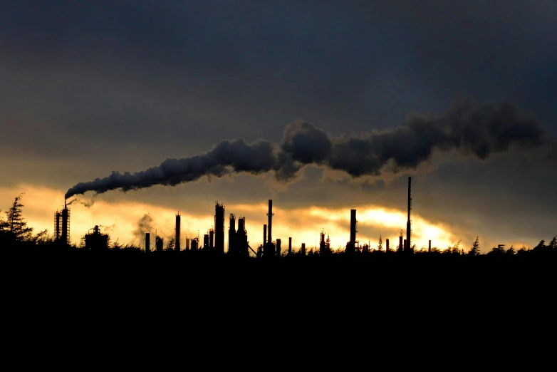 a line of chimneys billowing smoke as the sun is setting