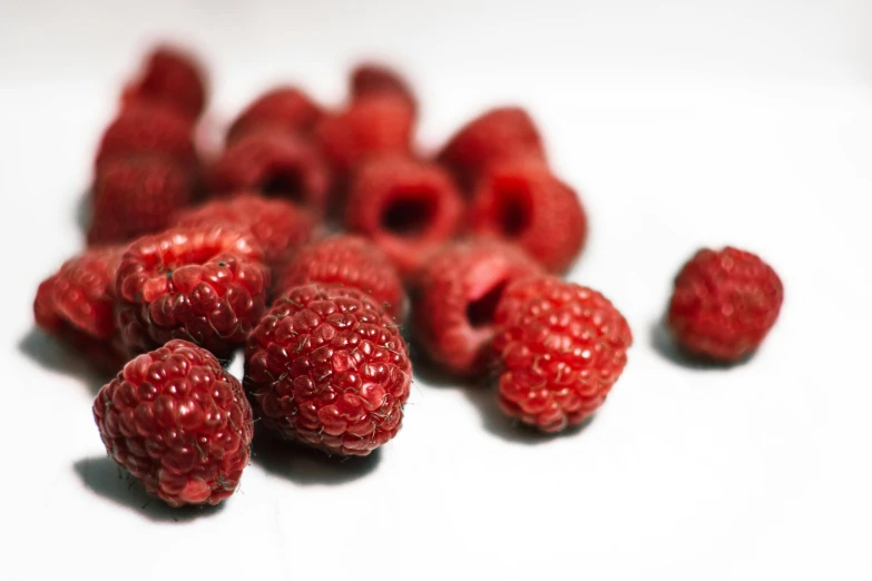 several different sized red raspberries on white surface