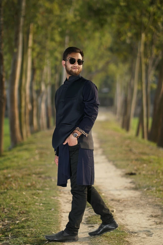 a man in sunglasses and a black coat stands on a dirt road