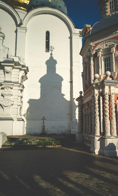 a small white building with a long shadow of the church