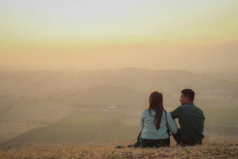 a man and woman sitting on a hill looking at the valley