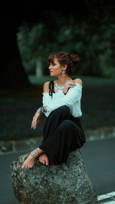 a woman wearing a necklace and long skirt posing on a rock