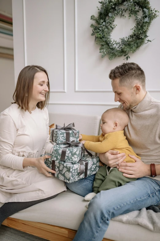 a young family holds their son as they sit on a couch with presents