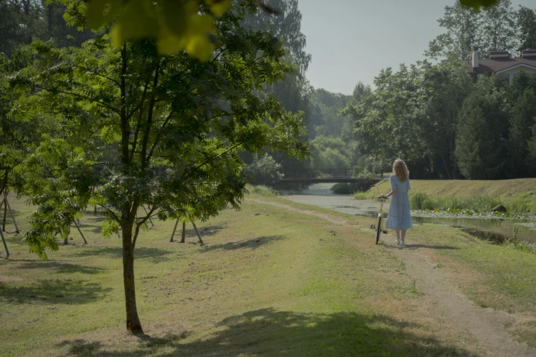 a woman is walking through the park with her bike