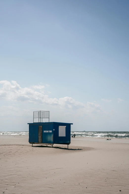 a little blue building sitting on the beach near the ocean