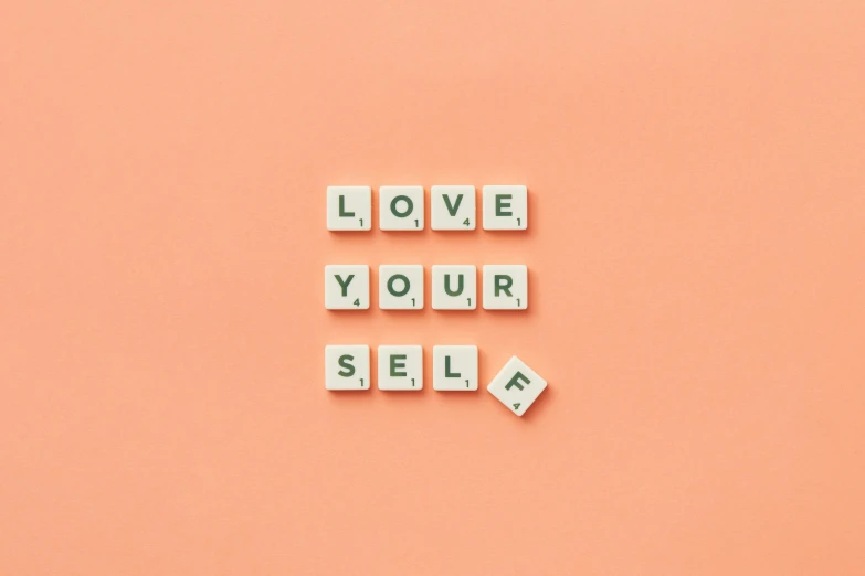 three words on tiles spelling love your self above a pink background