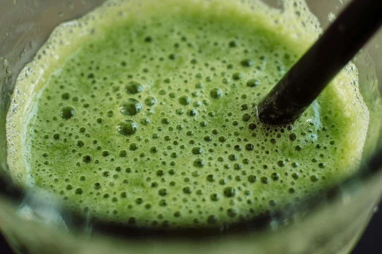 a black spoon stirring a green drink in a clear glass