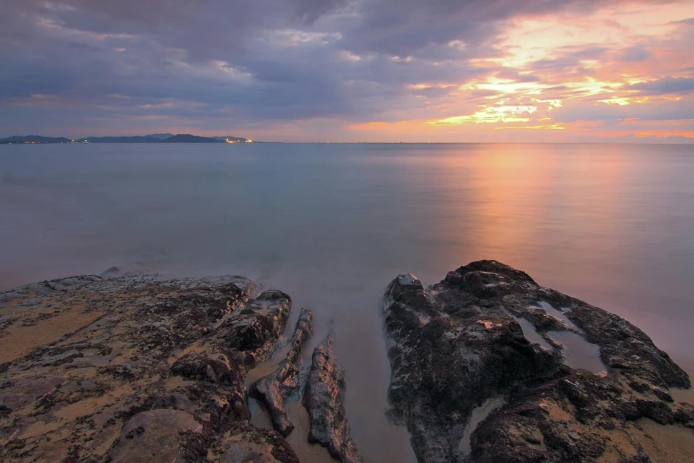 the sun setting over the water at a rocky shoreline