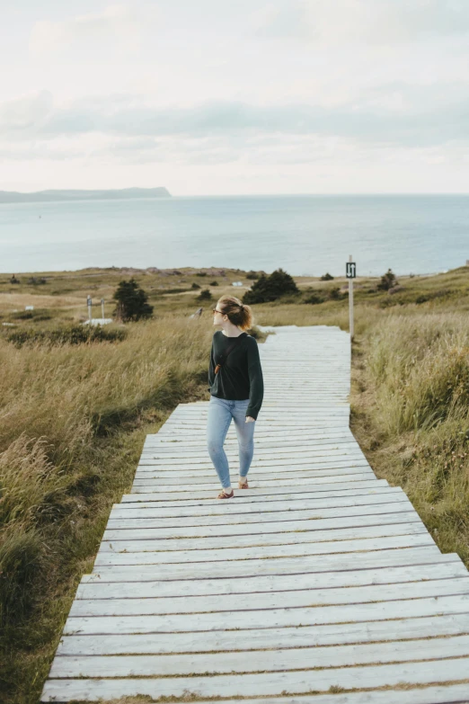 a woman standing on a bridge that is leading into the sea