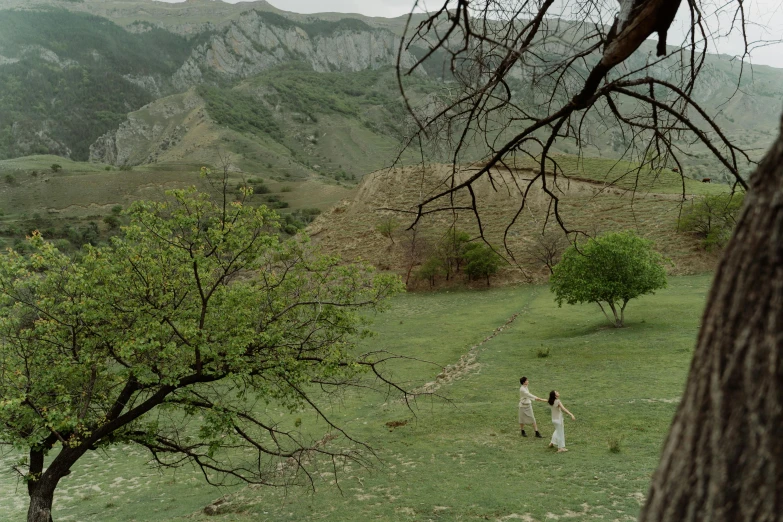 two people walk across a grassy field towards a mountain