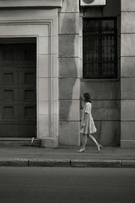 black and white pograph of a woman walking by an old building