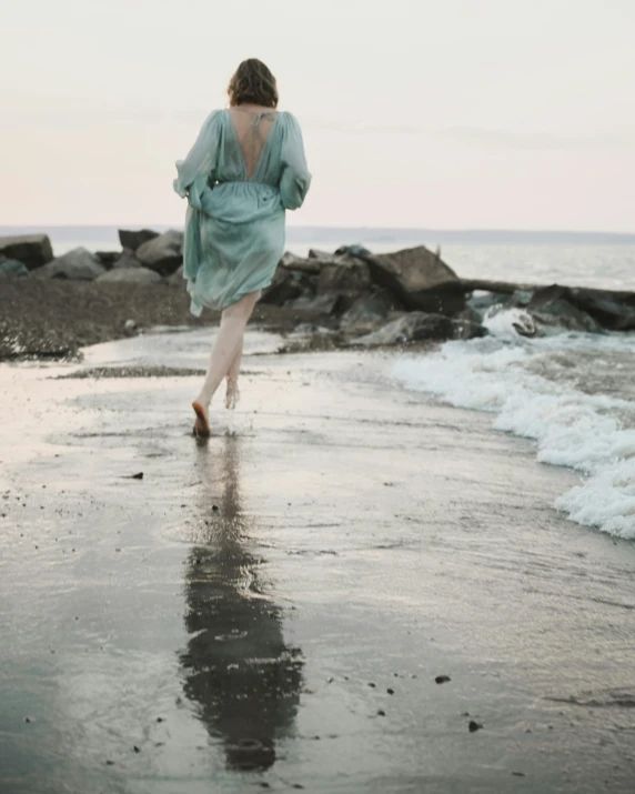 a woman in a blue shirt walking along the beach