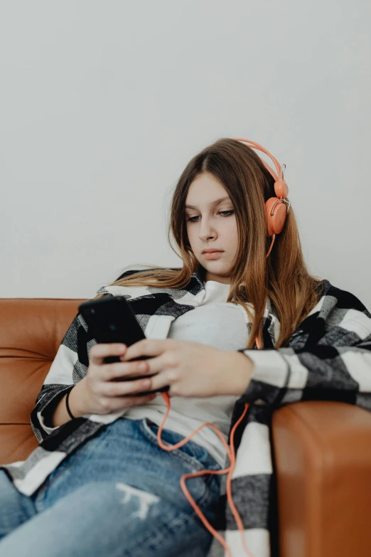 a young woman is sitting on a leather couch and listening to music with headphones