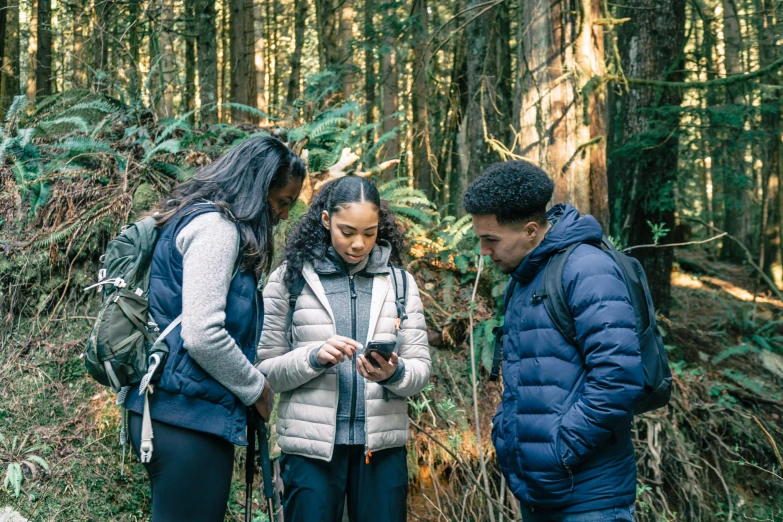 three people in the woods standing with a cell phone