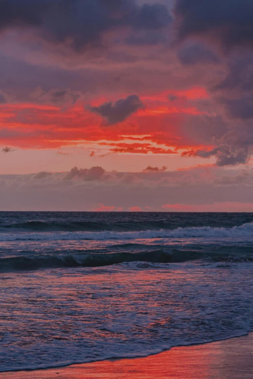 a surfer is walking on the beach to the ocean at sunset