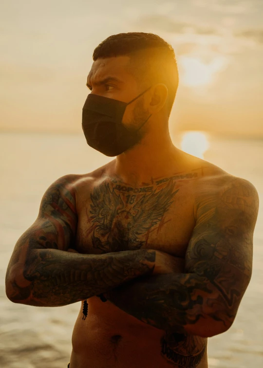 a man with a beard and tattooed arms standing by the ocean