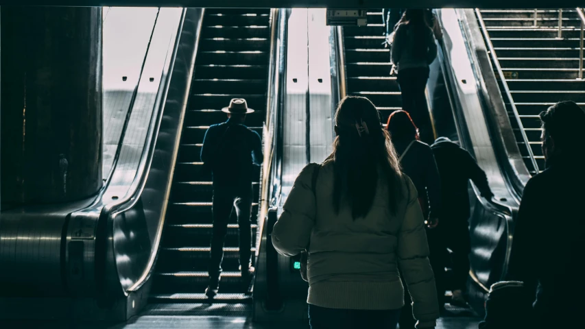 two women and one man are walking up an escalator