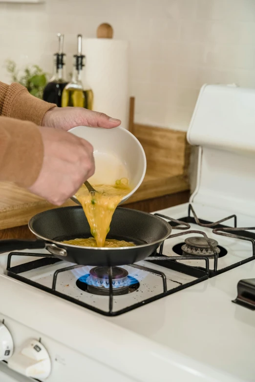 a person pouring cheese into a frying pan on a gas stove