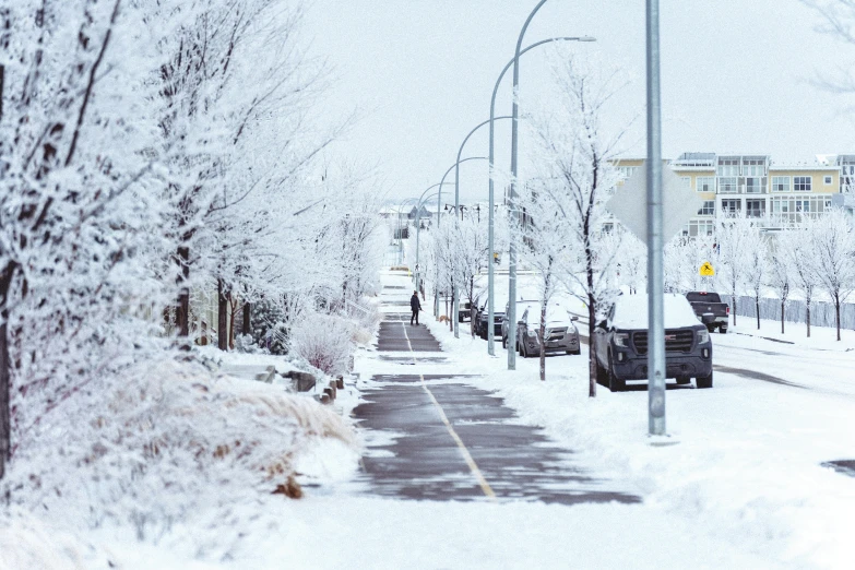 a snowy sidewalk on a residential street with parked cars