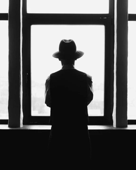 a man with a hat stands in front of a window