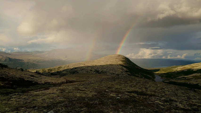 a single rainbow is in the distance over a small mountain