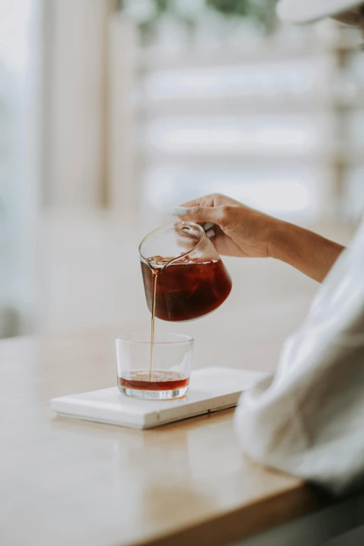 a person's hand pours liquid into a cup over a laptop