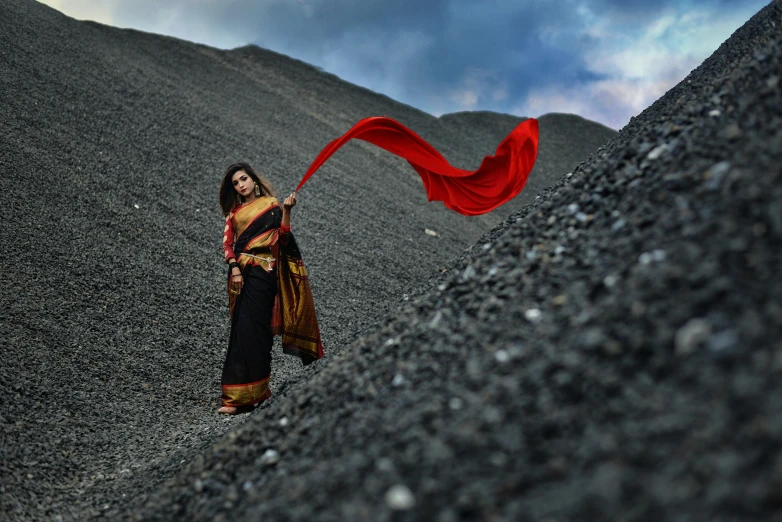 a woman holding a red scarf standing on a rocky hillside