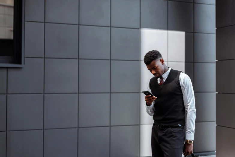 man in formal outfit standing with his hand in his pockets looking at his cellphone
