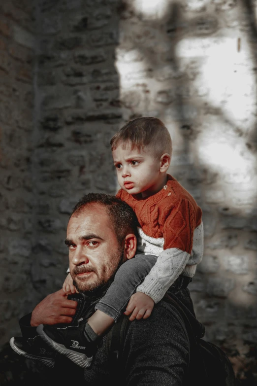 a man holding a small boy while standing in front of a stone wall