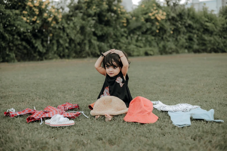 a toddler sitting on a grass field, putting her head down and grabbing her hands up