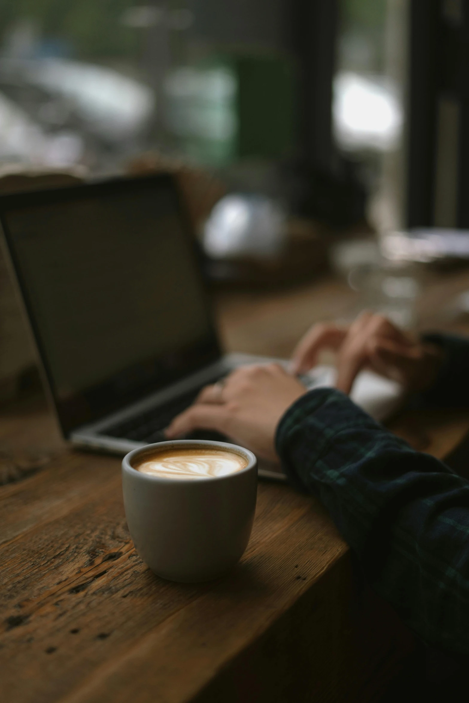 a person typing on their laptop next to a coffee cup