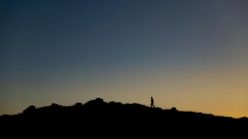 silhouette of person standing on a rocky hillside at sunset