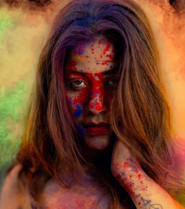 a woman covered in various colored powder holding her hands near her face