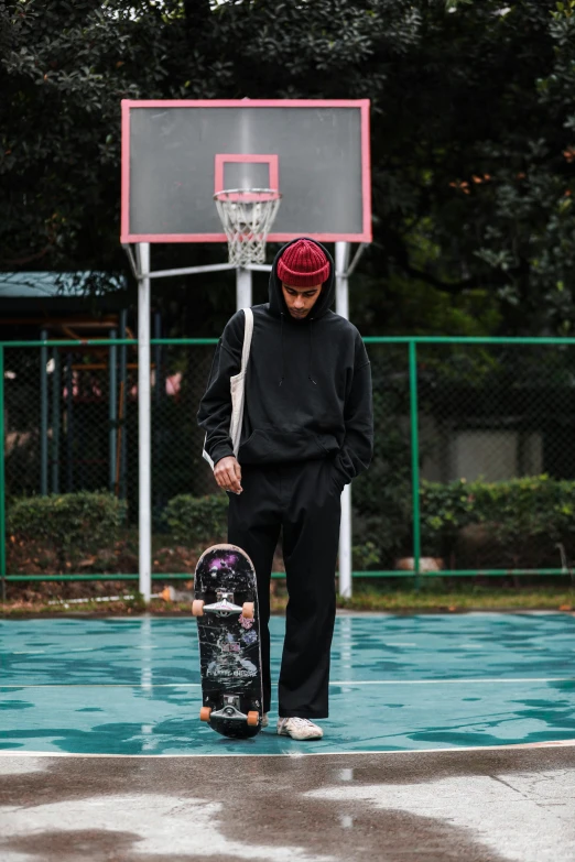 a young man carrying a skateboard near a basketball hoop