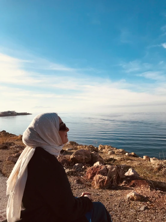 a woman sitting at the edge of a cliff next to the water