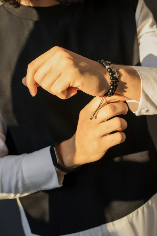 a young man tying his watch with a black beaded celet