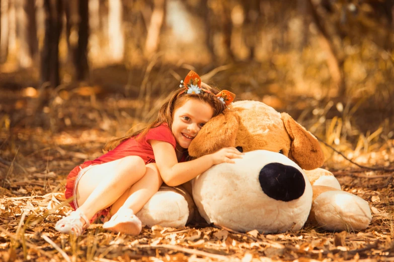 a little girl sitting next to a large stuffed dog in the woods