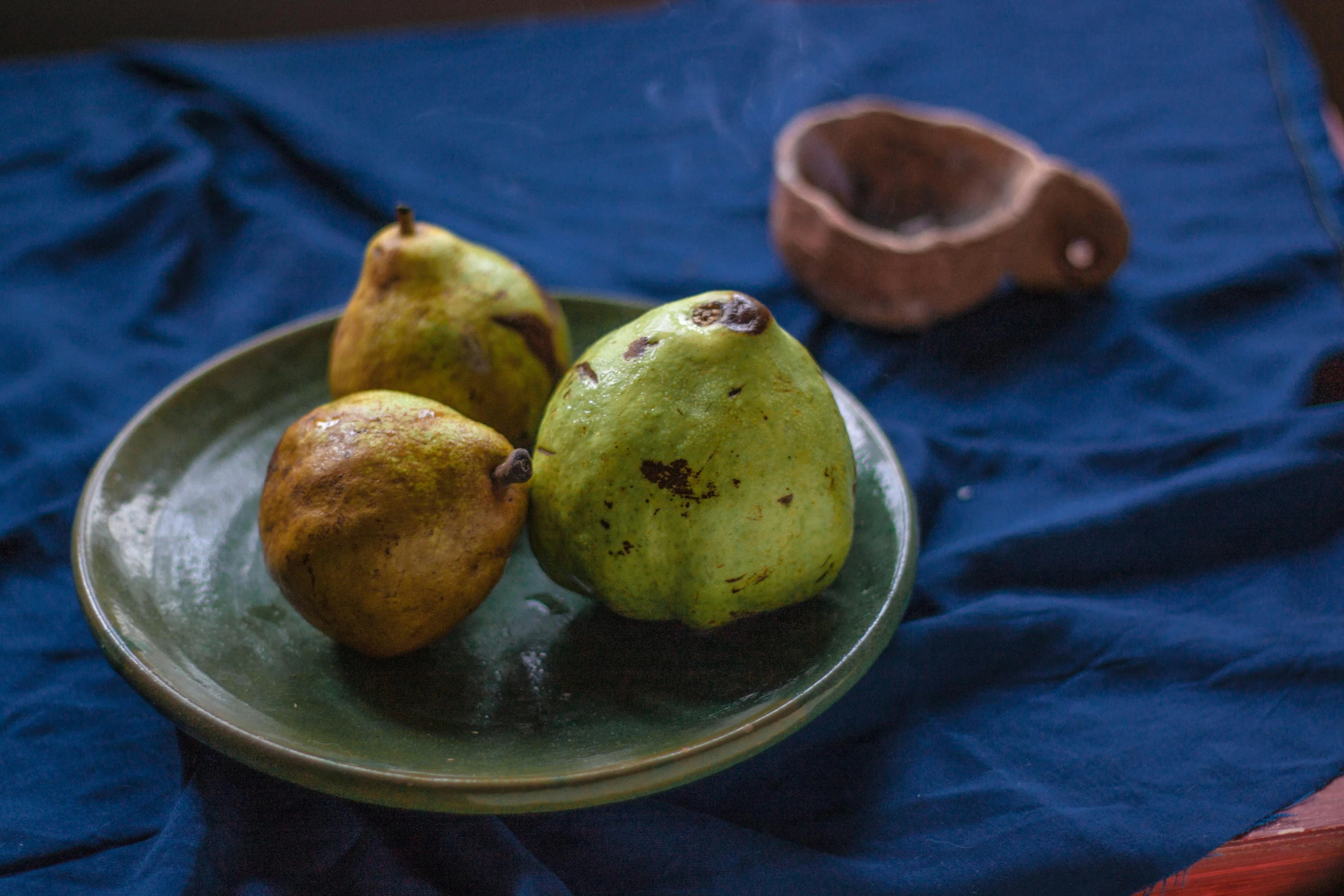 three pears and an empty bowl on blue cloth