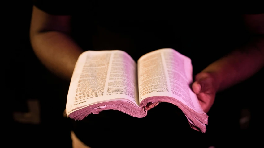 hands holding a bible with pink cloth on top of it
