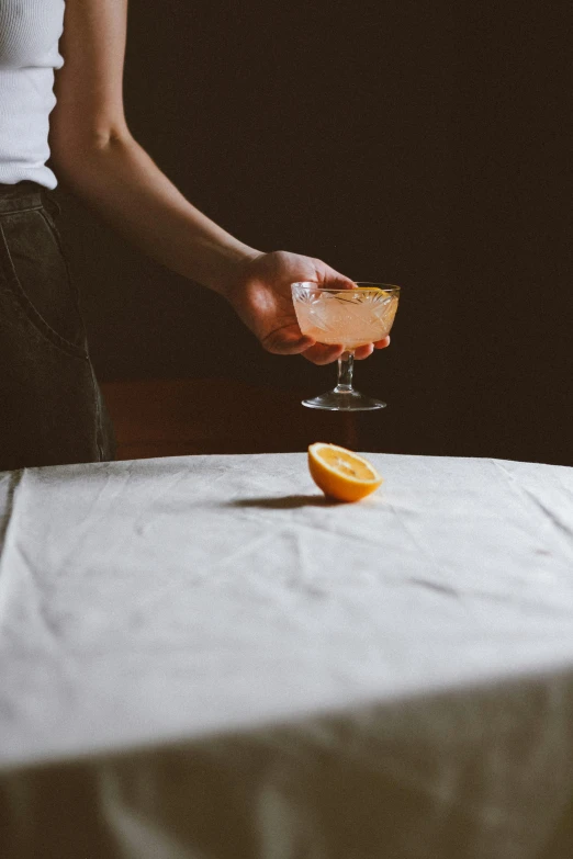 a woman holding up an orange to a drink