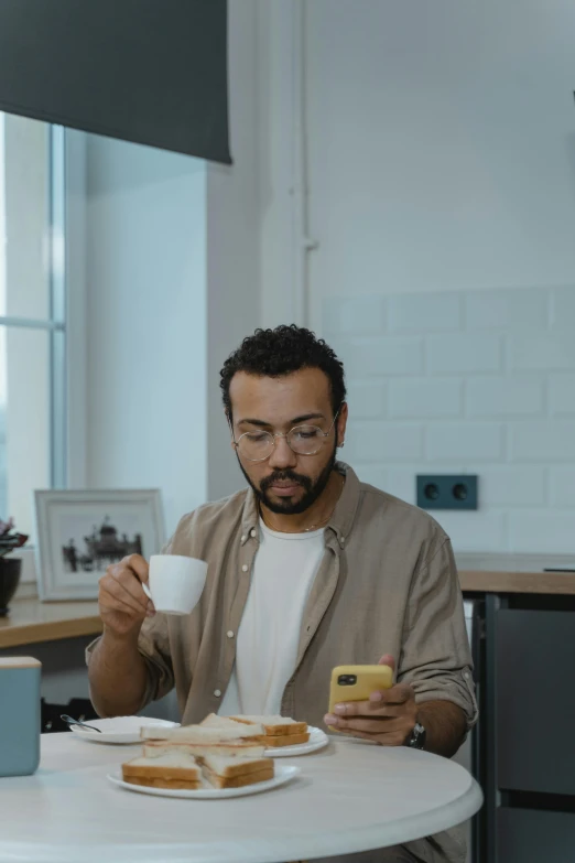 a man with eyeglasses on at a white table looking at a phone