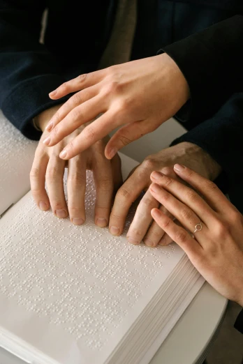 three people holding hands together over a book